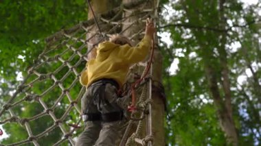 Bir güvenlik koşum küçük çocuk bir orman macera parkı bir rota üzerinde tırmanıyor. Yüksek halat patikalarına tırmanıyor. Zip hatları ve her türlü oluşan tırmanma faaliyetleri ile açık eğlence merkezi
