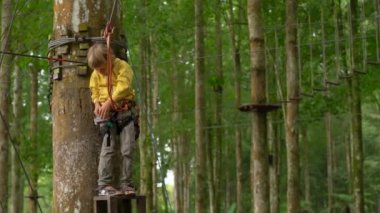 Bir güvenlik koşum küçük çocuk bir orman macera parkı ağaç tepelerinde bir zipline binmek için hazırlanıyor. Yüksek halat patikalarına tırmanıyor. Zip oluşan tırmanma faaliyetleri ile açık eğlence merkezi