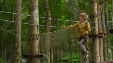 Bir güvenlik koşum küçük çocuk bir orman macera parkı ağaç tepelerinde bir rota üzerinde tırmanıyor. Yüksek halat patikalarına tırmanıyor. Zip hatları ve tüm oluşan tırmanma faaliyetleri ile açık eğlence merkezi
