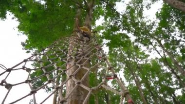 Bir güvenlik koşum küçük bir çocuk slowmotion çekim bir orman macera parkı ağaç tepelerinde bir rota üzerinde tırmanıyor. Yüksek halat patikalarına tırmanıyor. Tırmanma aktiviteleriyle açık hava eğlence merkezi