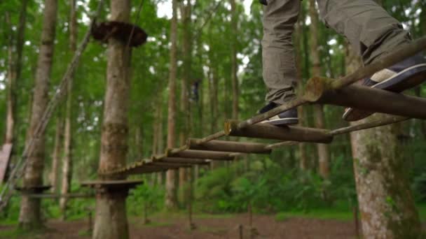 Superslowmotion shot van een jongetje in een veiligheidsharnas klimt op een route in boomtoppen in een forest Adventure Park. Hij klimt op een hoog touwparcours. Openlucht amusementscentrum met klimactiviteiten — Stockvideo