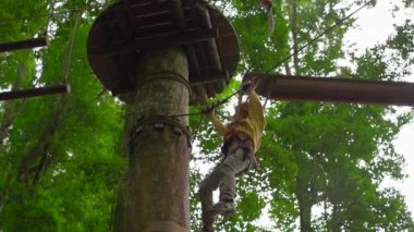Bir orman macera parkı ağaç tepelerinde bir zipline üzerinde bir güvenlik koşum küçük bir çocuk slowmotion çekim. Zip hatları ve her türlü oluşan tırmanma faaliyetleri ile açık eğlence merkezi