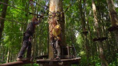 Bir orman macera parkı ağaç tepelerinde bir rota üzerinde bir güvenlik koşum tırmanmaya iki küçük çocuk Superslowmotion çekim. Yüksek halat patikalarına tırmanıyorlar. Tırmanma aktiviteleri ile açık hava eğlence merkezi