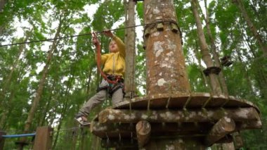 Bir güvenlik koşum küçük bir çocuk Superslowmotion çekim bir orman macera parkı ağaç tepelerinde bir rota üzerinde tırmanıyor. Yüksek halat patikalarına tırmanıyor. Tırmanma aktiviteleri ile açık hava eğlence merkezi