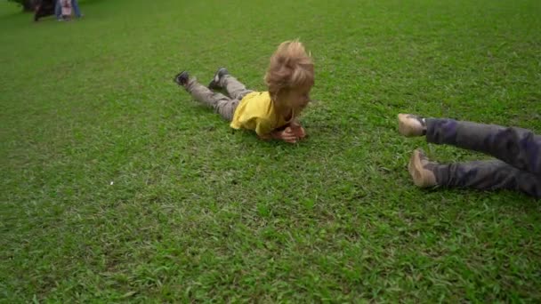 Superslowmotion shot of two little boys have fun on a lawn. They roll down the hill — Stock Video