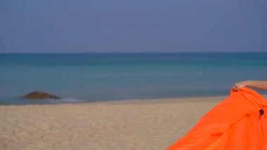 Tropik bir plajda genç bir kadın şişme kanepe şişirmek. Yaz tatili konsepti