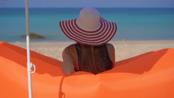 Zeitlupenaufnahme einer jungen Frau an einem tropischen Strand, die auf einem aufblasbaren Sofa sitzt. Sommerferienkonzept — Stockvideo