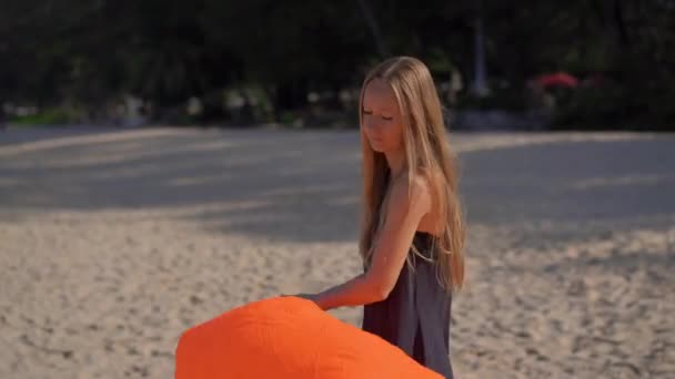 Jonge vrouw op een tropisch strand blazen een opblaasbare sofa. Zomer vakantie concept — Stockvideo