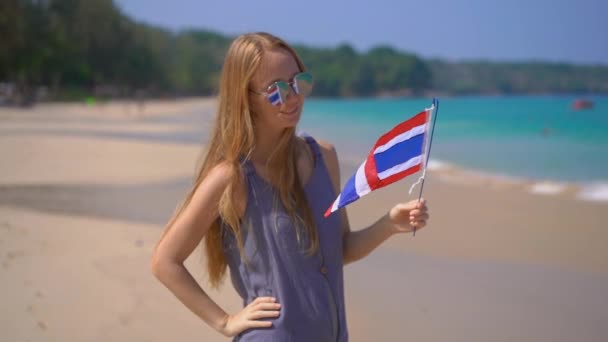 반사 선글라스를 착용한 아름다운 젊은 여성의 슈퍼 슬로우 모션 샷은 해변에 서있는 태국의 국기를 보유하고 — 비디오