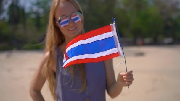 Superslowmotion disparo de una hermosa joven con gafas de sol reflectantes sostiene una bandera nacional de Tailandia de pie en una playa — Vídeos de Stock