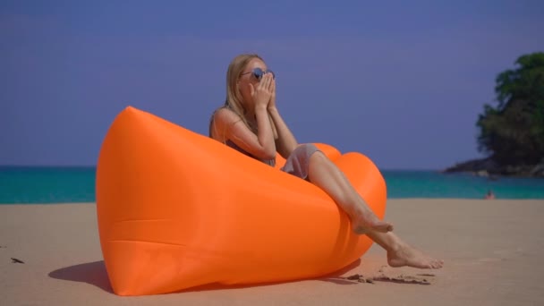 Суперснимок молодой женщины, кашляющей, сидя на раскладном диване на пляже. концепция болезни путешествий — стоковое видео