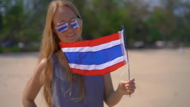 Superslowmotion tiro de uma bela jovem mulher vestindo um óculos de sol reflexivo mantém uma bandeira nacional da Tailândia de pé em uma praia — Vídeo de Stock
