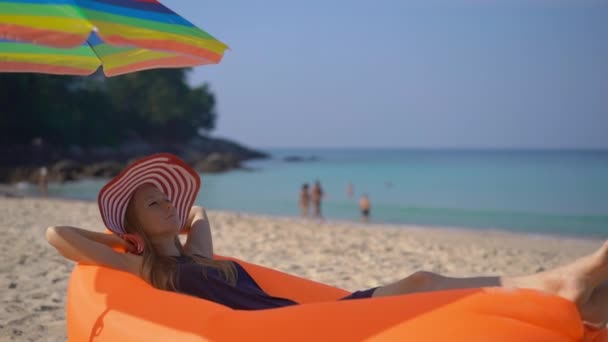 Superzeitlupenaufnahme einer jungen Frau an einem tropischen Strand, die sich auf ein aufblasbares Sofa legt. Sommerferienkonzept — Stockvideo