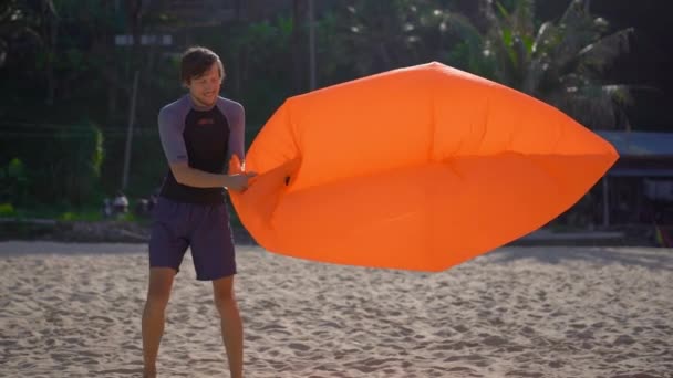 Superslowmotion shot of a young man on a tropical beach inflates an inflatable sofa. Summer vacation concept — Stock Video