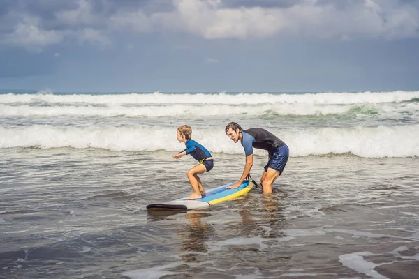 Padre o instructor enseñando a su hijo de 5 años cómo surfear en el mar de vacaciones o vacaciones. Viajes y deportes con concepto infantil. Clases de surf para niños — Foto de Stock