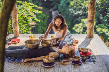 Spa salonunda Nepal Buda bakır kasesi. Genç, güzel bir kadın masaj terapisi yapıyor. Spa 'da şelaleye karşı kâseler söylüyor. Ses terapisi, dinlenme, meditasyon, sağlıklı yaşam tarzı ve...