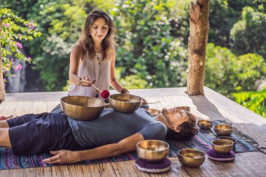 Spa salonunda Nepal Buda bakır şarkı kase. Genç güzel adam bir şelale karşı Spa'da şarkı kase masaj terapisi yapıyor. Ses terapisi, rekreasyon, meditasyon, sağlıklı yaşam tarzı ve vücut