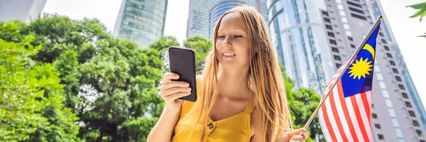 Viajes y tecnología. Mujer joven turista con la bandera de Malasia está viendo un mapa de la ciudad en un teléfono inteligente para la navegación BANNER, FORMATO LARGO —  Fotos de Stock