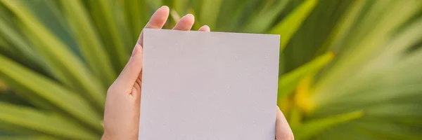 Womens hands in a tropical background holding a signboard paper, mockup BANNER, LONG FORMAT — Stock Photo, Image