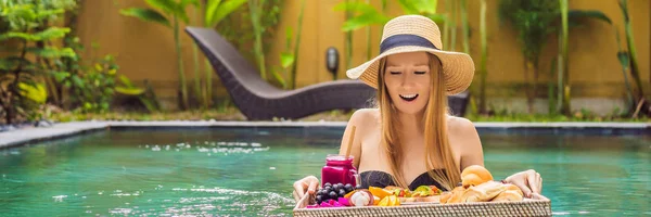 BANNER, LONG FORMAT Breakfast tray in swimming pool, floating breakfast in luxury hotel. Girl relaxing in the pool drinking smoothies and eating fruit plate, smoothie bowl by the hotel pool. Exotic