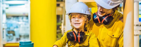 BANNER, FORMATO LARGO Joven y un niño pequeño llevan un uniforme de trabajo amarillo, gafas y casco en un entorno industrial, plataforma petrolera o planta de gas licuado — Foto de Stock