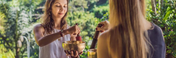 BANNER, FORMATO LARGO Nepal Cuenco de cobre de Buda en el salón de spa. Joven hermosa mujer haciendo terapia de masaje cantando cuencos en el Spa contra una cascada. Terapia de sonido, recreación, meditación —  Fotos de Stock