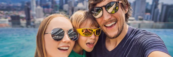 Vacanza e tecnologia. Famiglia felice con bambino che prende selfie insieme vicino alla piscina con vista panoramica sulla città BANNER, FORMATO LUNGO — Foto Stock