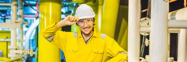 Mladý muž ve žluté pracovní uniformě, brýle a přilba v průmyslovém prostředí, ropná plošina nebo zařízení na zkapalněný plyn nápis, dlouhý formát — Stock fotografie