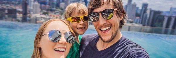 Vacanza e tecnologia. Famiglia felice con bambino che prende selfie insieme vicino alla piscina con vista panoramica sulla città BANNER, FORMATO LUNGO — Foto Stock