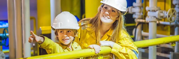 Mujer joven y un niño pequeño son ambos en un uniforme de trabajo amarillo, gafas y casco en un entorno industrial, Plataforma de petróleo o planta de gas licuado BANNER, FORMATO LARGO — Foto de Stock