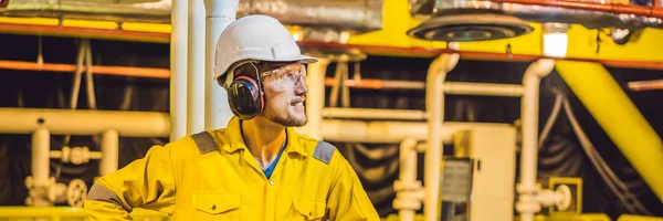Young man in a yellow work uniform, glasses and helmet in industrial environment,oil Platform or liquefied gas plant BANNER, LONG FORMAT — Stock Photo, Image