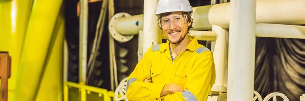 Mladý muž ve žluté pracovní uniformě, brýle a přilba v průmyslovém prostředí, ropná plošina nebo zařízení na zkapalněný plyn nápis, dlouhý formát — Stock fotografie