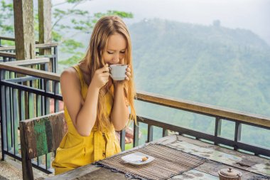 Genç kadın dağlarda bir kafede kahve içiyor