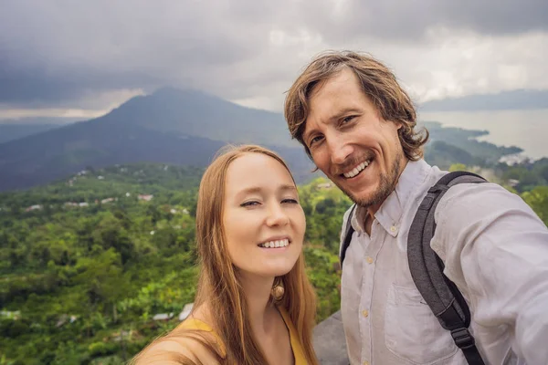 Hombre y mujer haciendo selfie en el fondo del volcán Batur y la vista de la montaña Agung en la mañana desde Kintamani, Bali, Indonesia —  Fotos de Stock