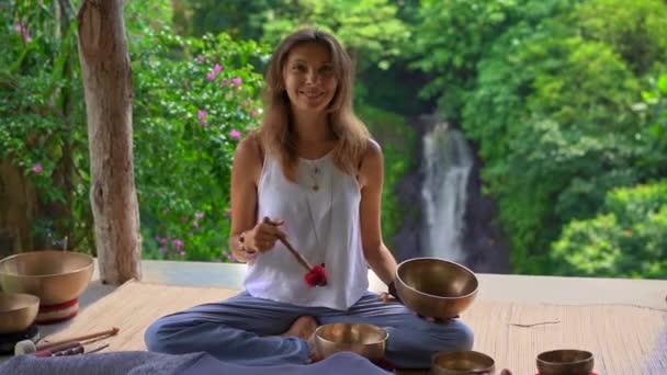 Superslowmotion shot of a woman master of Asian sacred medicine performs Tibetan bowls healing ritual for a client young woman. Meditation with Tibetan singing bowls. They are in a gazebo for — Stock Video