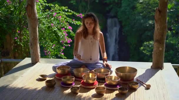 Superslowmotion plan d'une femme maître de la médecine sacrée asiatique effectue des bols tibétains rituel de guérison. Méditation avec bols chantants tibétains. Elle est assise dans un gazebo pour la méditation avec une belle — Video
