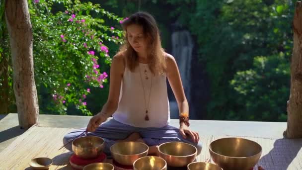 Superslowmotion shot of a woman master of Asian sacred medicine performs Tibetan bowls healing ritual. Meditation with Tibetan singing bowls. She sits in a gazebo for meditation with a beautiful — Stock Video