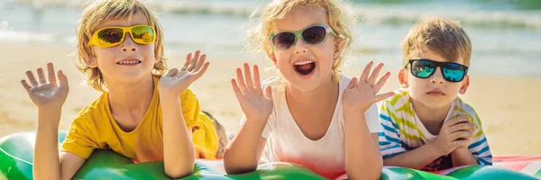 I bambini si siedono su un materasso gonfiabile in occhiali da sole contro il mare e si divertono BANNER, FORMATO LUNGO — Foto Stock