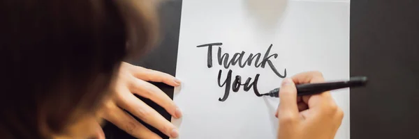 BANNER, LONG FORMAT Thank you. Calligrapher Young Woman writes phrase on white paper. Inscribing ornamental decorated letters. Calligraphy, graphic design, lettering, handwriting, creation concept