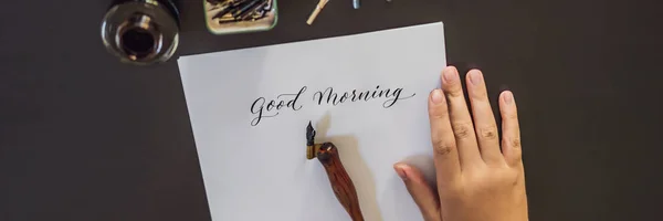 Banner, lang formaat Goedemorgen. Kalligraaf jonge vrouw schrijft zin op wit papier. Inscribing sier versierde letters. Kalligrafie, grafisch ontwerp, belettering, handschrift, creatie concept — Stockfoto