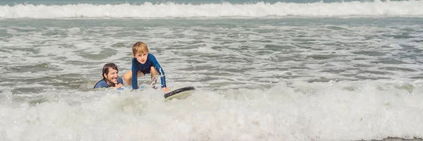 BANNER, LONG FORMAT Father or instructor teaching his 5 year old son how to surf in the sea on vacation or holiday. Travel and sports with children concept. Surfing lesson for kids