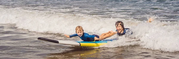 BANNER, LONG FORMAT Father or instructor teaching his 5 year old son how to surf in the sea on vacation or holiday. Travel and sports with children concept. Surfing lesson for kids