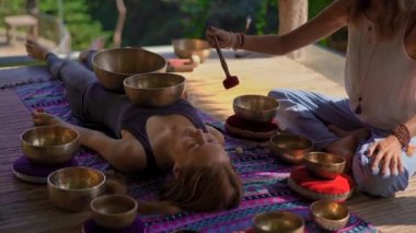 Asya kutsal tıp bir kadın ustası Superslowmotion atış bir müşteri genç kadın için Tibet kase şifa ritüel gerçekleştirir. Tibet şarkı kaseleri ile Meditasyon. Onlar için bir çardak bulunmaktadır