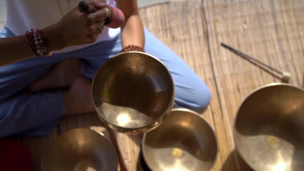 Superslowmotion skott av en kvinna mästare i asiatisk helig medicin utför tibetanska skålar helande ritual. Meditation med tibetanska sjungande skålar. Hon sitter i ett lusthus för meditation med en vacker — Stockvideo