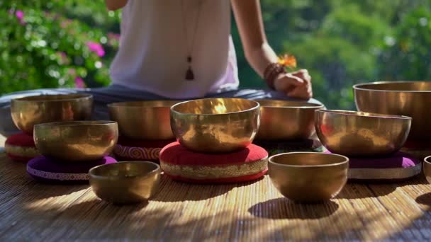 Superslowmotion shot of a woman master of Asian sacred medicine performs Tibetan bowls healing ritual. Meditation with Tibetan singing bowls. She sits in a gazebo for meditation with a beautiful — Stock Video
