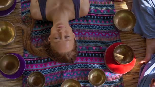 Сверхнизкий кадр женщины-мастера азиатской священной медицины выполняет тибетский ритуал исцеления чаш для клиентки молодой женщины. Медитация с тибетскими чашами для пения. Они находятся в газировке для — стоковое видео