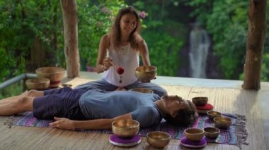Asya kutsal tıp bir kadın ustası Superslowmotion atış bir müşteri genç adam için Tibet kase şifa ritüel gerçekleştirir. Tibet şarkı kaseleri ile Meditasyon. Meditasyon için çardaktalar.