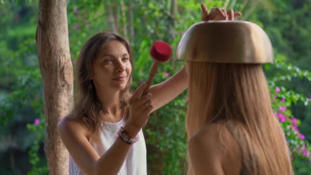 Superslowmotion disparo de una mujer maestra de la medicina sagrada asiática realiza cuencos tibetanos ritual de curación para una joven cliente. Meditación con cuencos tibetanos. Están en un mirador para — Vídeos de Stock