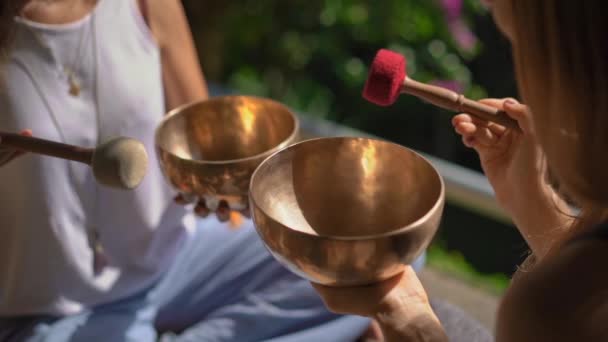 Superslowmotion skott av en kvinna mästare i asiatisk helig medicin utför tibetanska skålar helande ritual för en klient ung kvinna. Meditation med tibetanska sjungande skålar. De är i ett lusthus för — Stockvideo