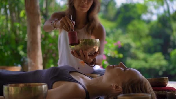 Superslowmotion disparo de una mujer maestra de la medicina sagrada asiática realiza cuencos tibetanos ritual de curación para una joven cliente. Meditación con cuencos tibetanos. Están en un mirador para — Vídeo de stock